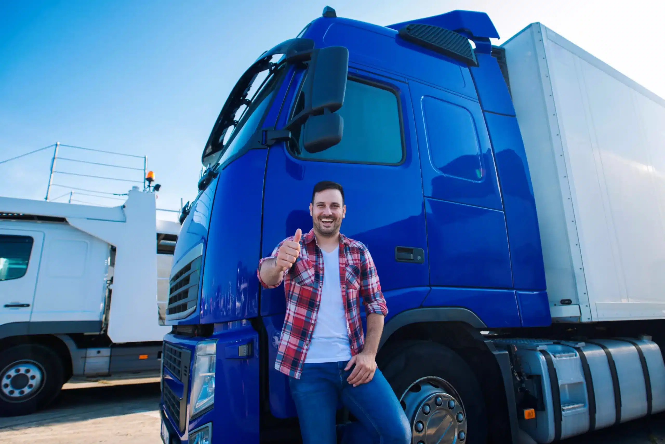 kamionista s úsmevom na tvári drží palec hore a opiera sa o modrý kamión